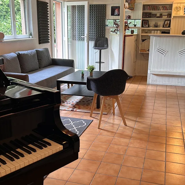 Le piano à queue au premier plan, ouvrant sur le coin salon et la cuisine de la pièce de vie du studio